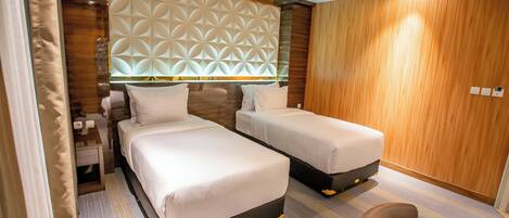 A hotel room with two beds, a wooden headboard, a small desk, and a chair.