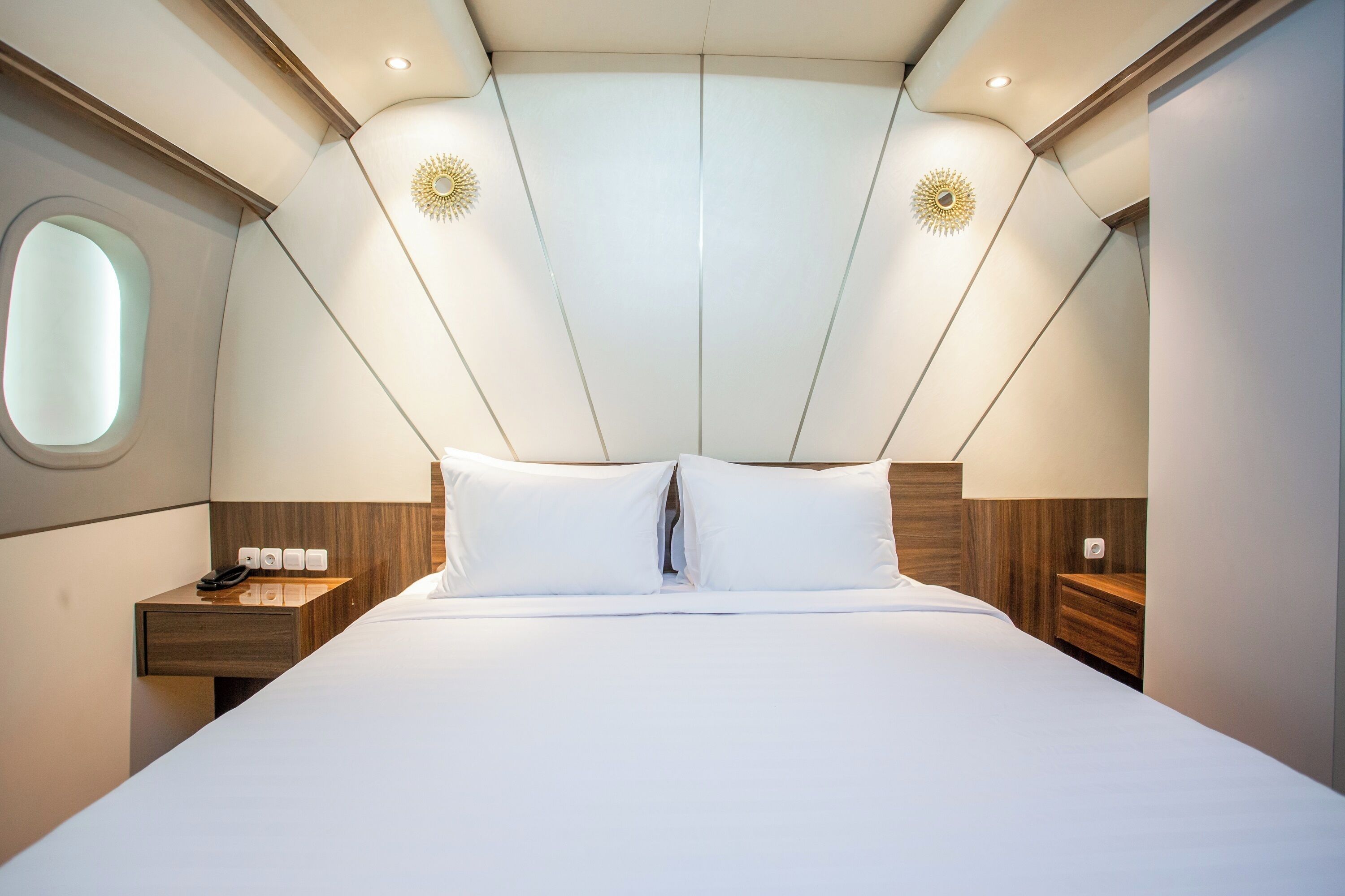 Une chambre d’hôtel moderne avec un grand lit, une tête de lit en bois et une petite table de chevet avec une lampe.