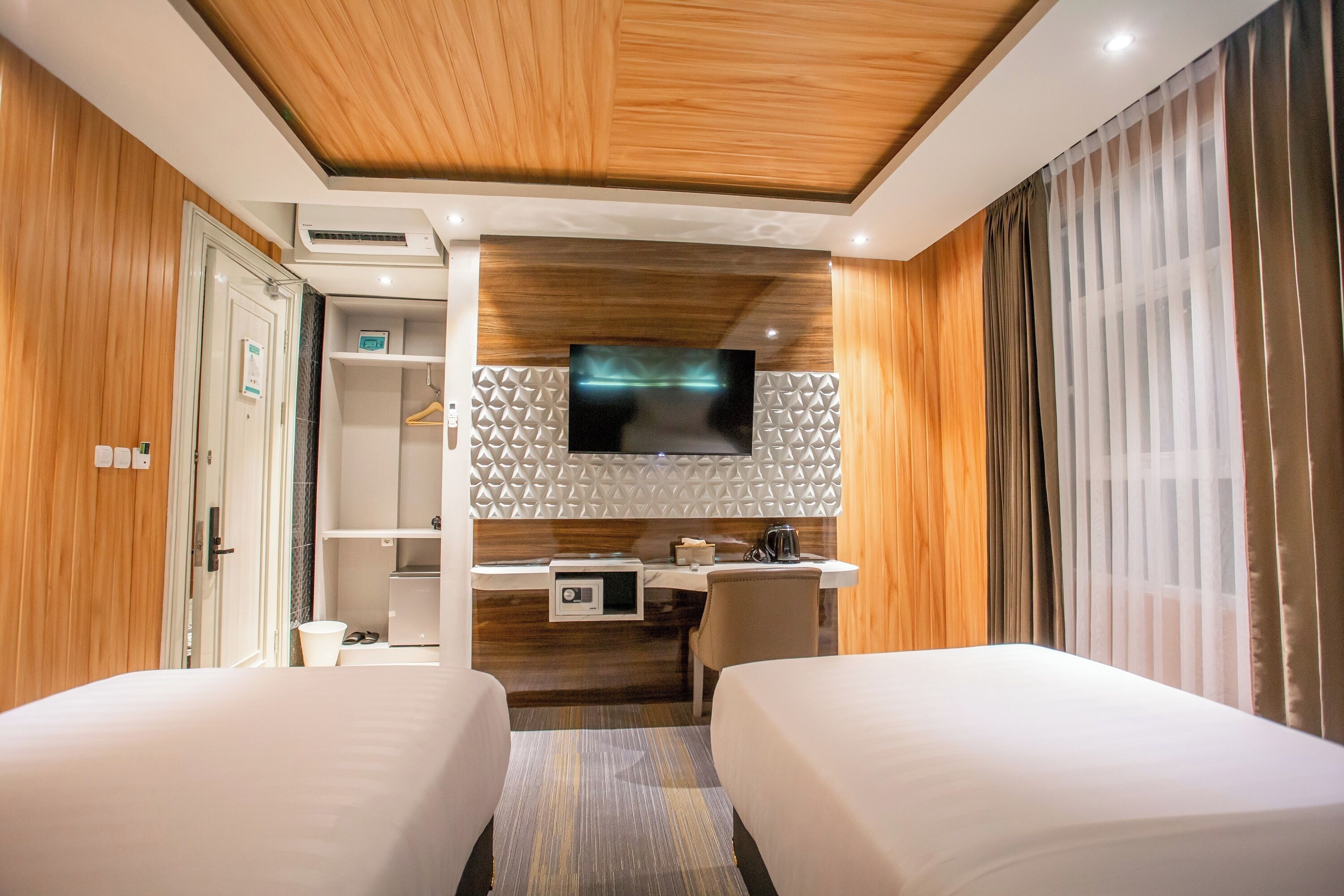 A hotel room with two beds, a desk with a flat-screen TV, a wardrobe, and a shower area.