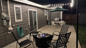 En baghavepatio med bålfæstebord, udendørsstole og lyskæder.