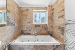 Ein modernes Badezimmer mit einer freistehenden Badewanne, Fliesen aus Naturstein, einem Fenster und einem Handtuchhalter.