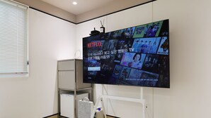 Une pièce avec un grand téléviseur fixé au mur qui diffuse différents contenus, un meuble blanc et une petite poubelle.