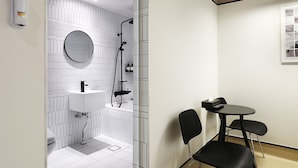Une salle de bain moderne avec une douche, un lavabo et des toilettes. On y trouve une petite table avec des chaises et un tableau encadré au mur.