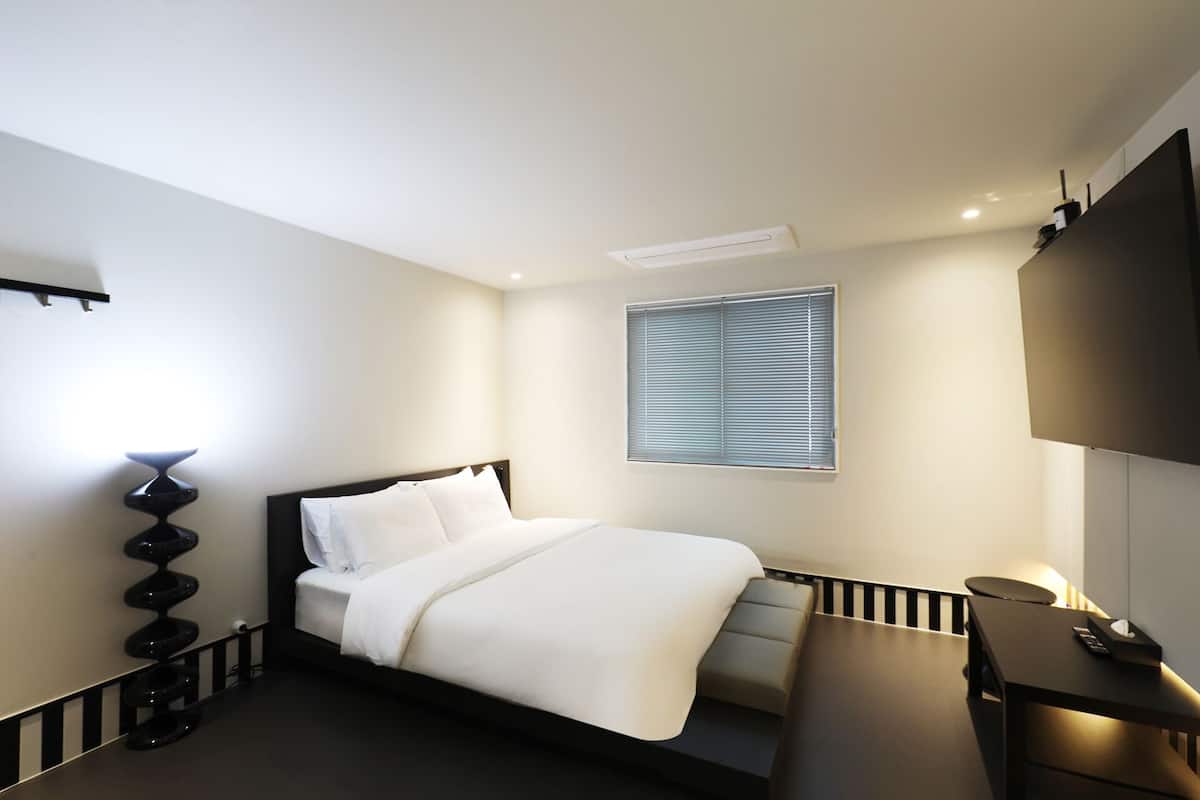 Une chambre d’hôtel moderne avec un lit bien fait, un petit bureau et un téléviseur fixé au mur.