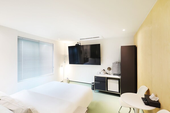 Une chambre d’hôtel moderne équipée d’un lit, d’un bureau, d’une chaise, d’une télévision et d’une armoire.