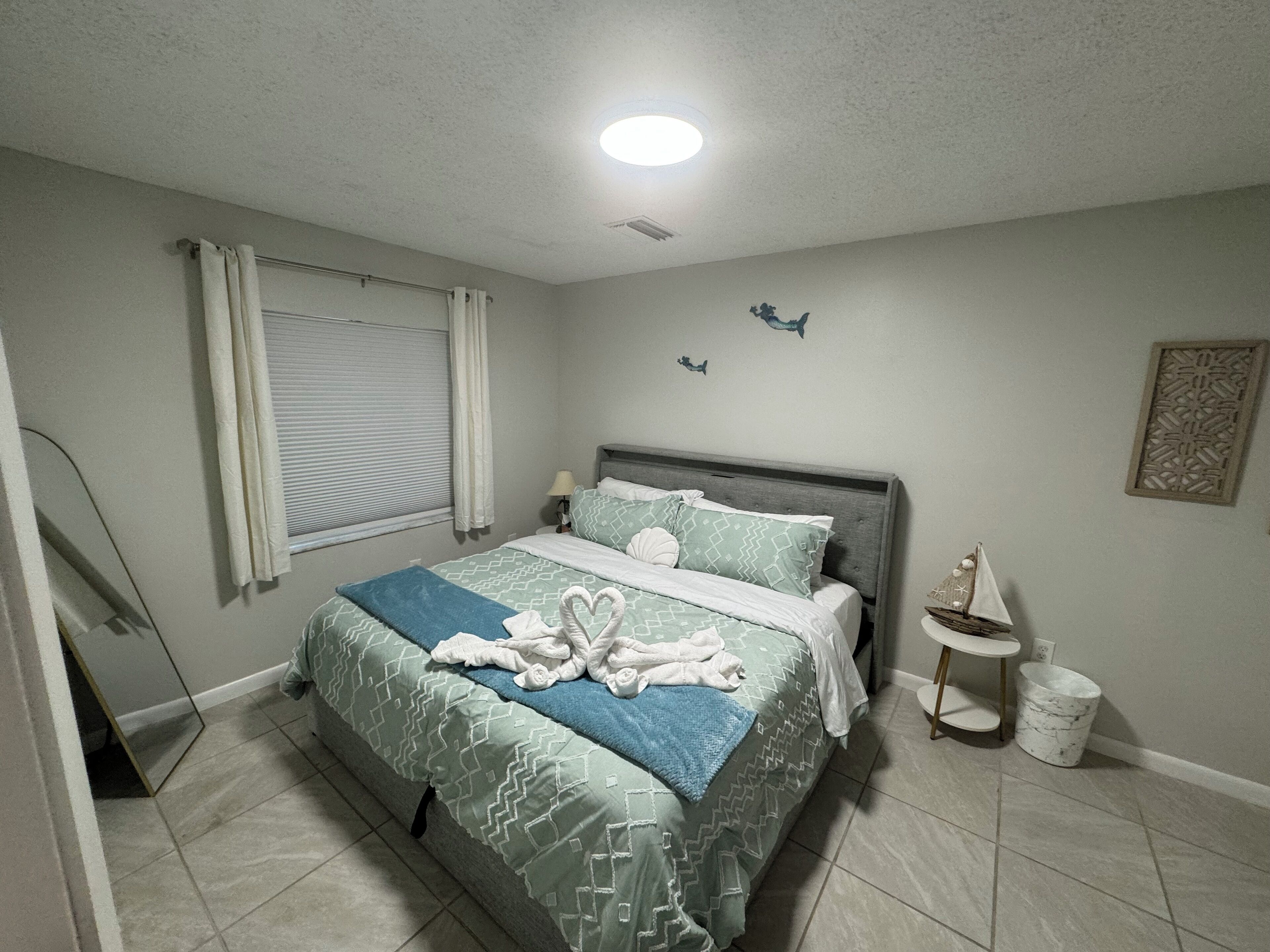 A bedroom with a bed, a nightstand, a lamp, a decorative wall piece, and a small shelf with a decorative item.