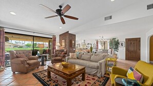 A spacious living room with a ceiling fan, a brick fireplace, and a large window offering a view of a golf course.