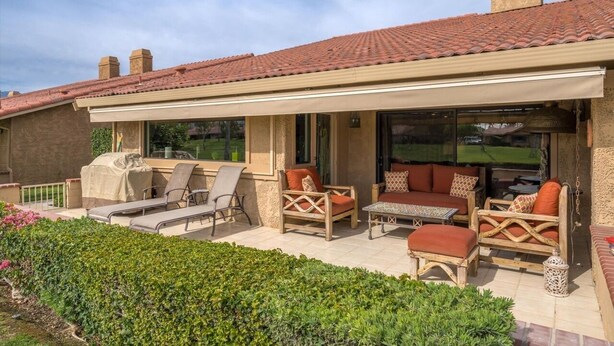 An outdoor patio with lounge chairs, a covered seating area, and a grill.