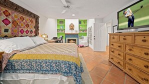 A bedroom with a bed, a television, a ceiling fan, a fireplace, and a bookshelf.