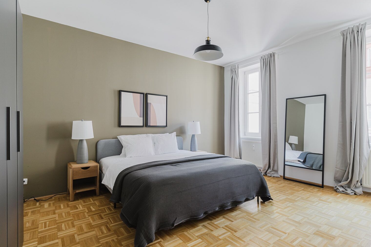 Un dormitorio con cama, lámparas de noche, un espejo y una ventana con cortinas.