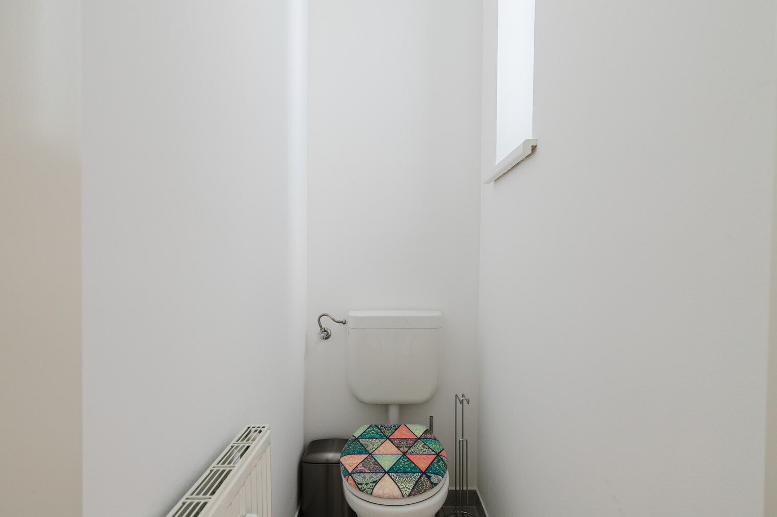 Un baño pequeño y estrecho con inodoro blanco y un radiador.