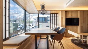 Um interior moderno com uma grande mesa de jantar, assentos, uma televisão e vista para montanhas nevadas.