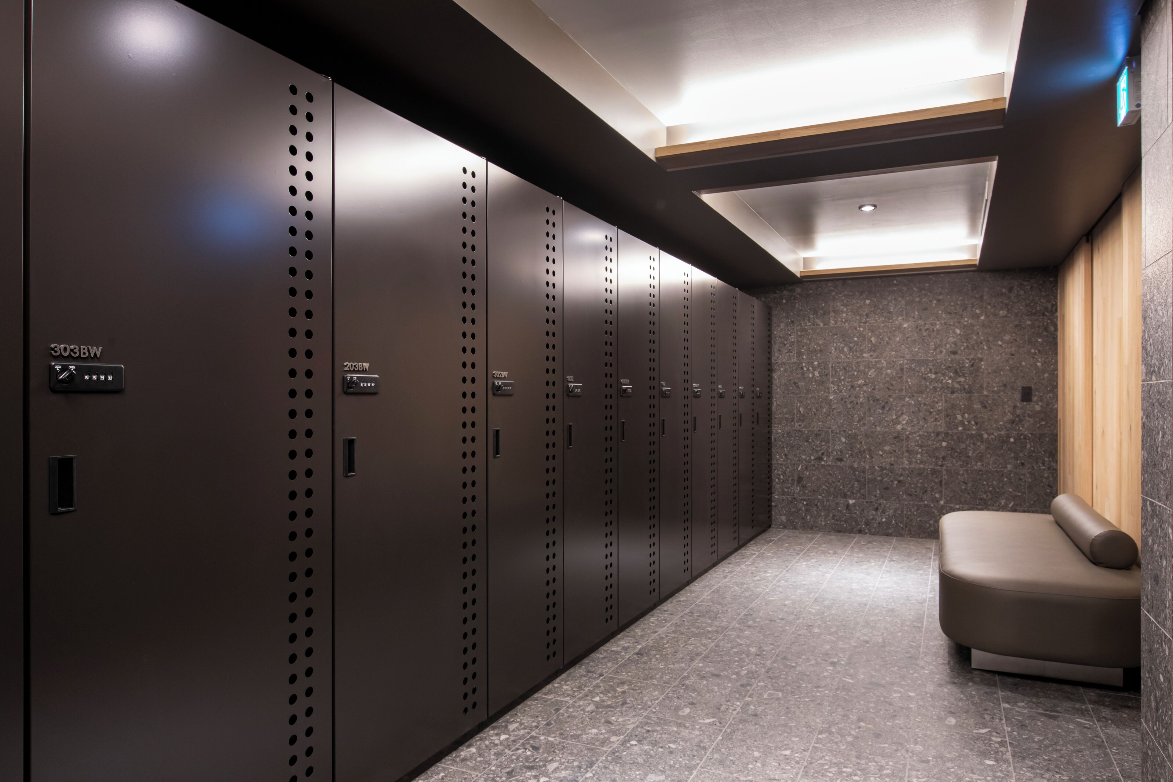 A modern locker room with multiple lockers, a bench, and a tiled floor.