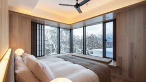 Quarto moderno com uma cama grande, ventoinha no teto e janelas amplas com vista para árvores cobertas de neve.