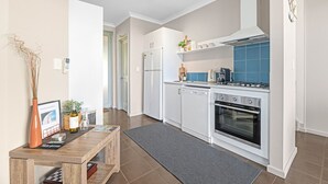 A modern kitchen with white cabinets, a stove, and a dishwasher. There is a wooden table with a vase and a picture frame. - Luxurious 2-Bedroom Spa Apartment with Ocean Views (KRONKUP)