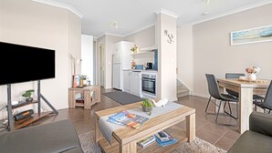 A modern living room with a flat-screen TV, a wooden coffee table, and a dining area with a table and chairs. - Luxurious 2-Bedroom Spa Apartment with Ocean Views (KRONKUP)