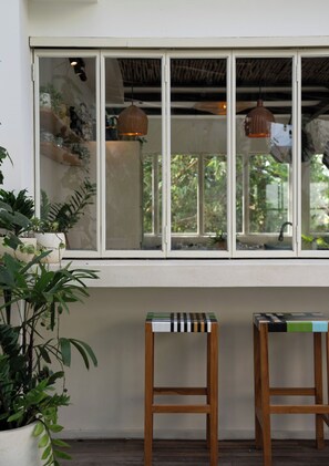 A window with two wooden stools in front, a shelf with plants, and hanging pendant lights. - Balai Amaia (Canggu)