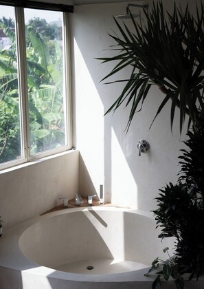 A bathroom with a bathtub, a window, and a potted plant. - Balai Amaia (Canggu)