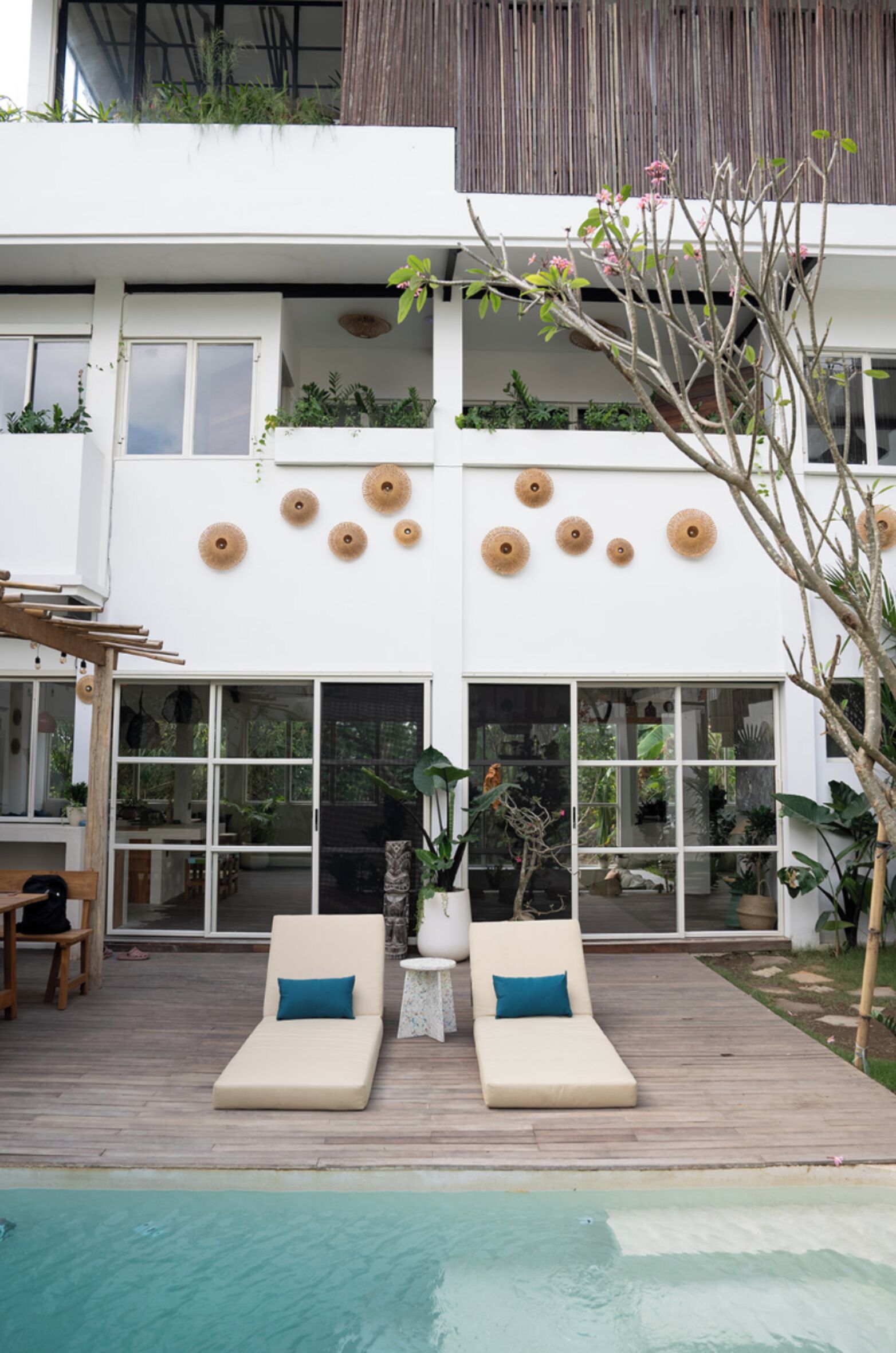 A modern house with a pool, two lounge chairs, and a wooden deck.