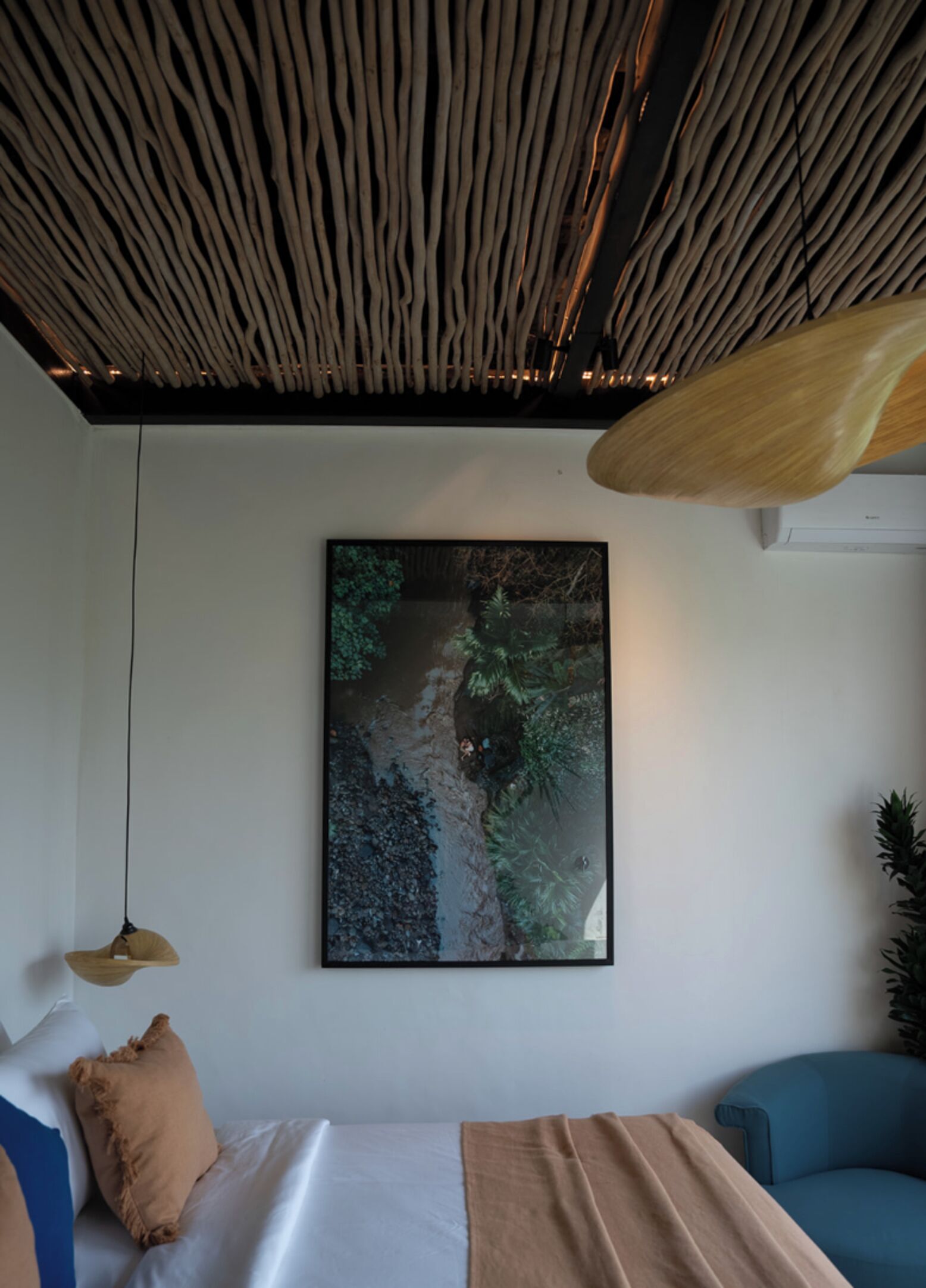 Ett modernt sovrum med en säng, en blå fåtölj, en hängande lampa och ett stort konstverk på väggen med naturmotiv.
