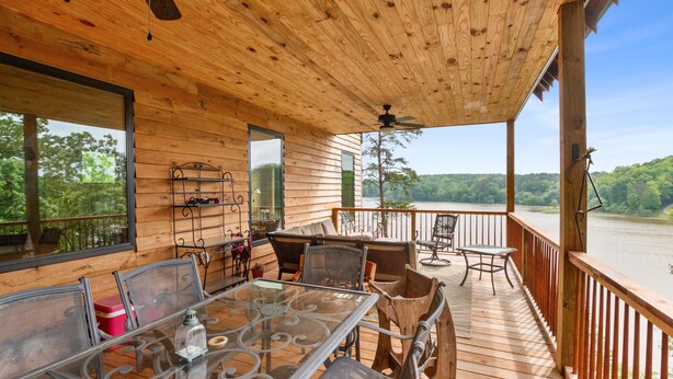 Una terraza de madera con muebles de exterior, una mesa de vidrio y vista a un lago.