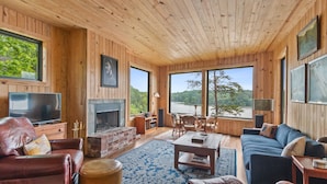 Un salón con paneles de madera, chimenea, muebles de cuero y ventanas amplias con vistas al exterior.