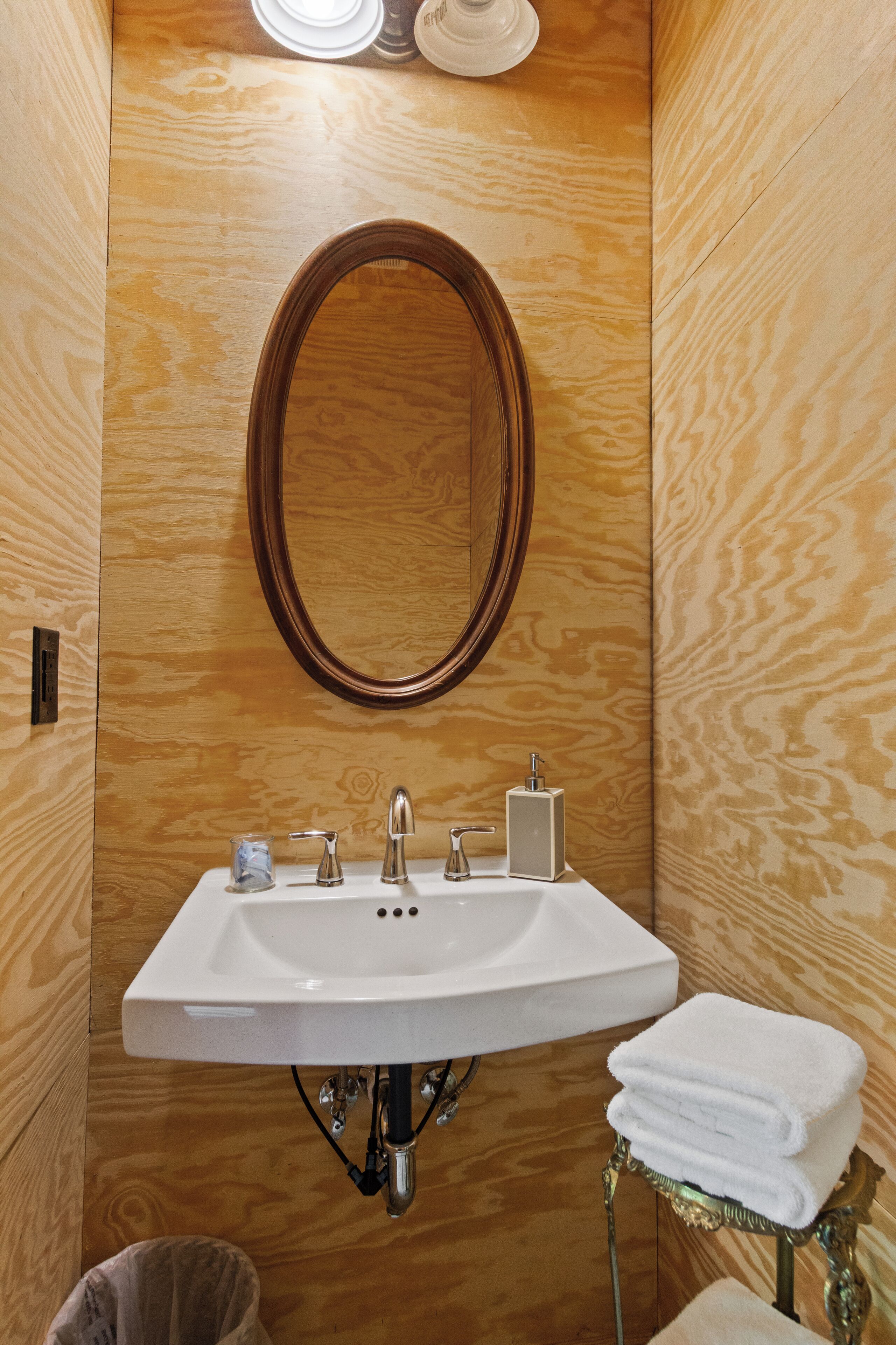 Ein Badezimmer mit Holzwand, einem weißen Waschbecken mit Spiegel darüber und einem Stapel weißer Handtücher auf einem kleinen Tisch.