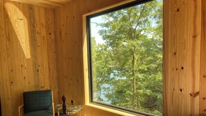 Una habitación de madera con un ventanal grande, una cama, una silla y una pequeña mesa.