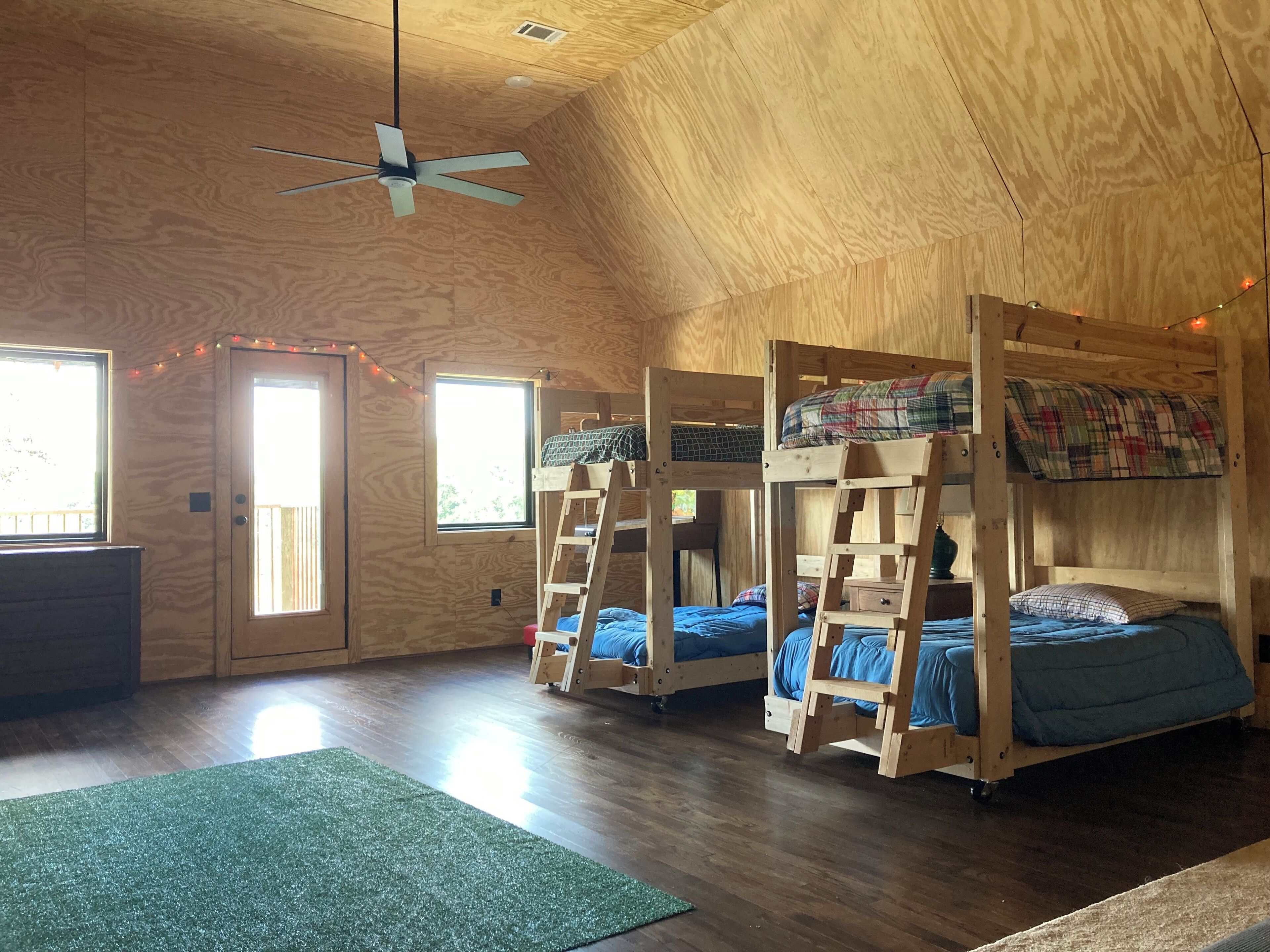 A room with three bunk beds, a ceiling fan, and a window with curtains.