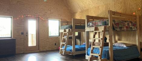 Une chambre avec trois lits superposés, un ventilateur de plafond et une fenêtre avec des rideaux.