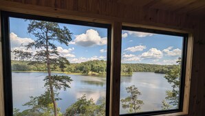 Una habitación con dos amplios ventanales que ofrecen vistas a un lago rodeado de árboles y colinas.