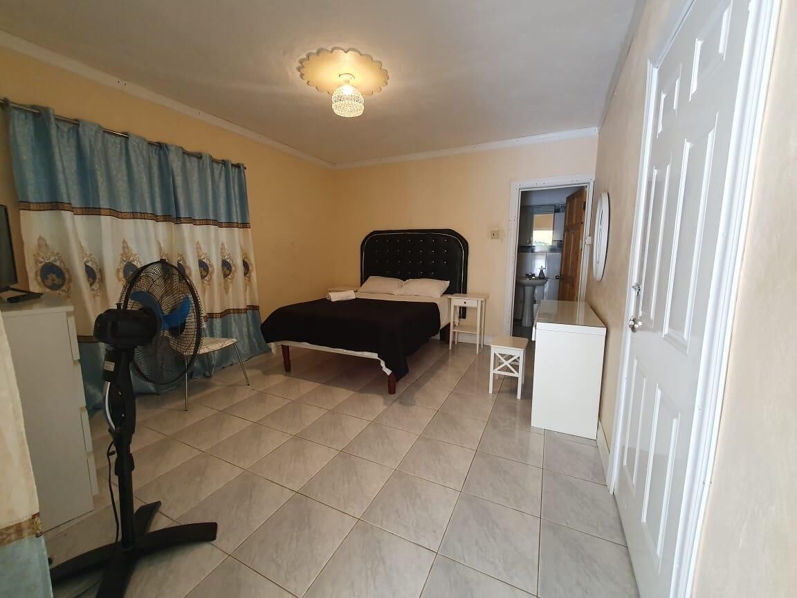 A bedroom with a bed, bedside table, and a standing fan.