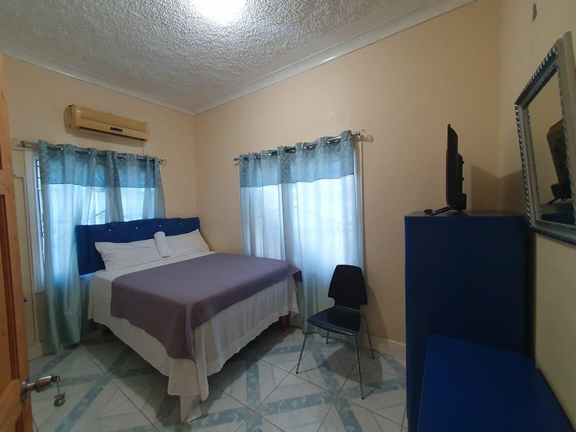 A bedroom with a bed, a chair, a desk, and a mirror.
