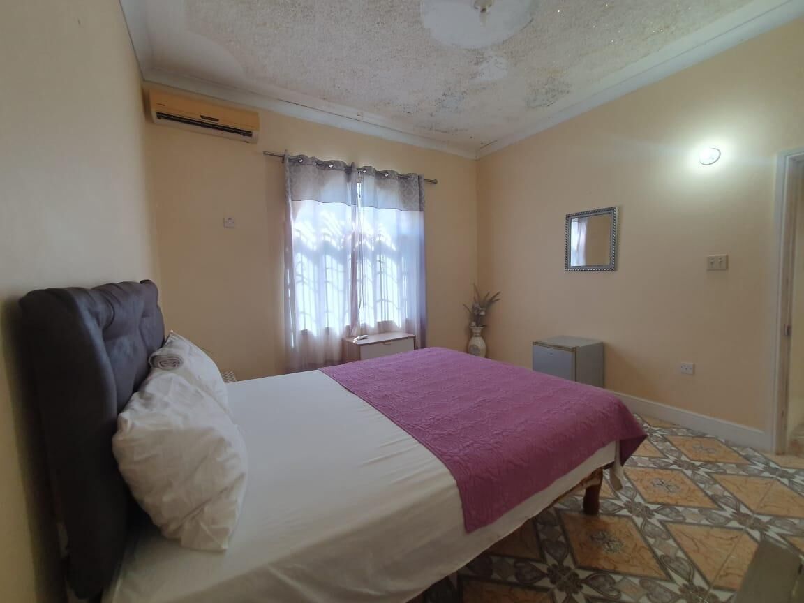 Une chambre à coucher avec un lit, une table de chevet, un miroir et une fenêtre avec des rideaux.