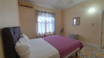 Une chambre à coucher avec un lit, une table de chevet, un miroir et une fenêtre avec des rideaux.