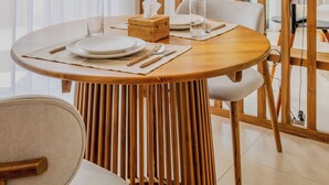 A dining area with a round wooden table, white chairs, and a woven light fixture.