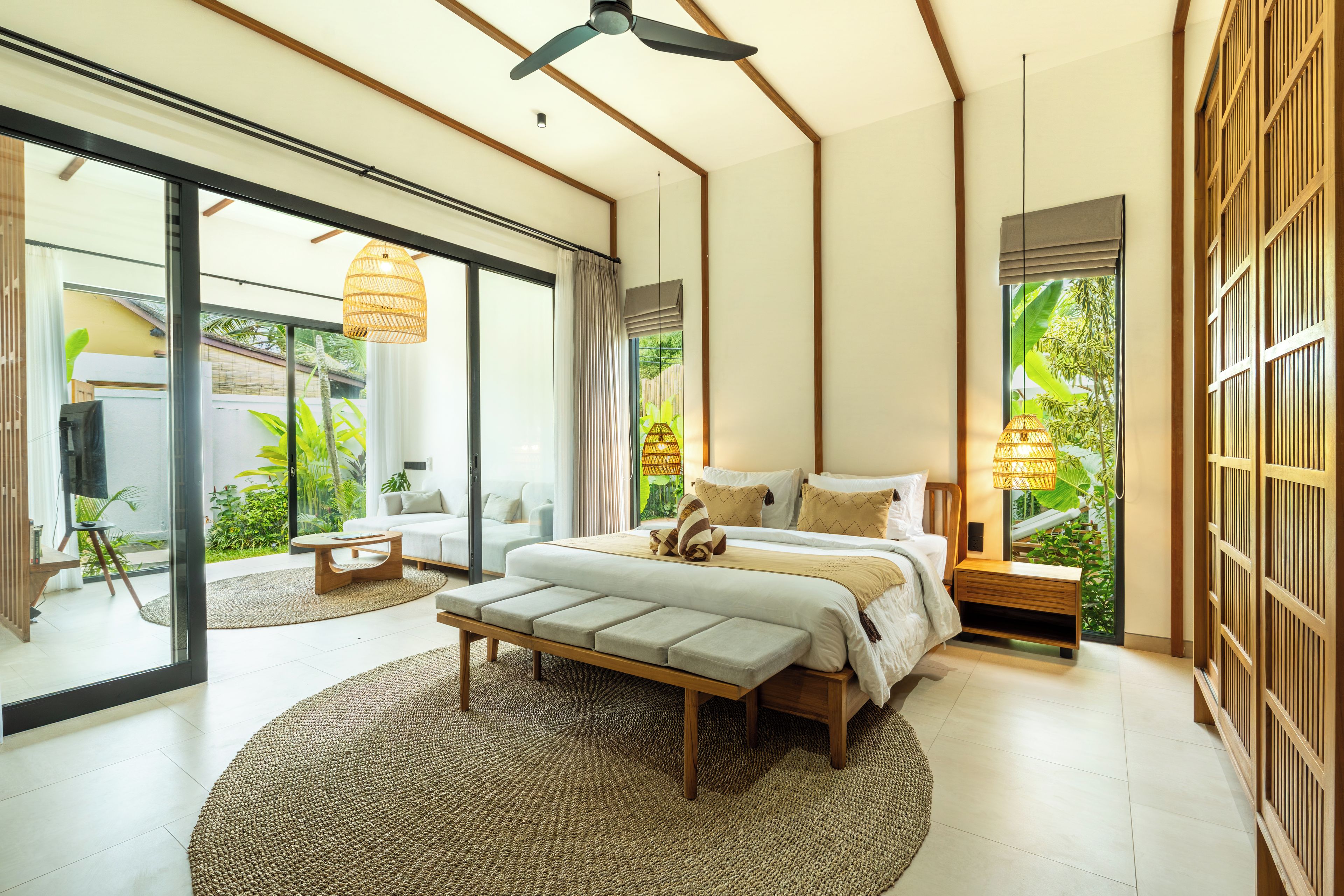A modern bedroom with a large bed, a bench, and a view of greenery outside.