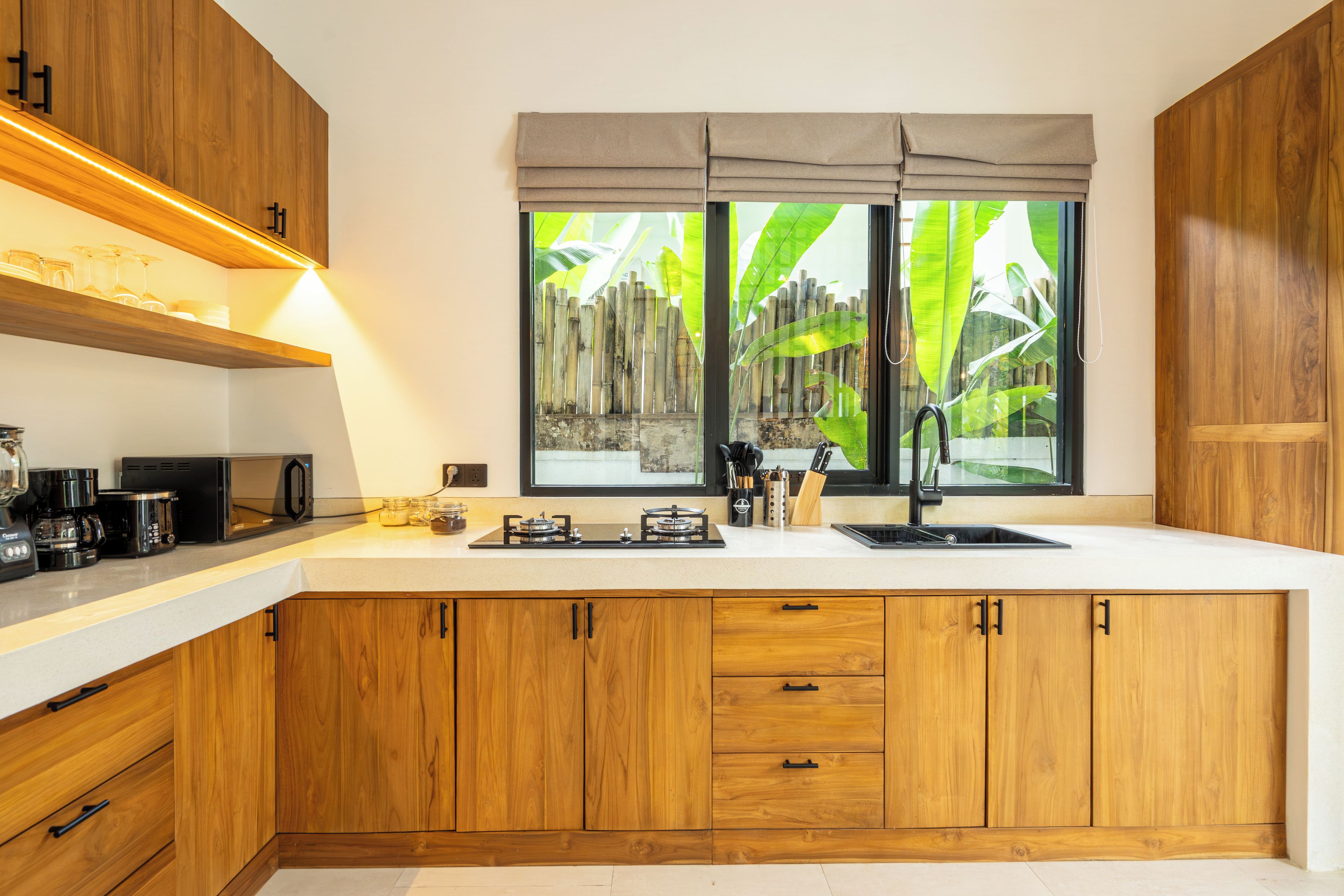 Cozinha moderna com armários de madeira, bancada branca e janela com vista para o verde.
