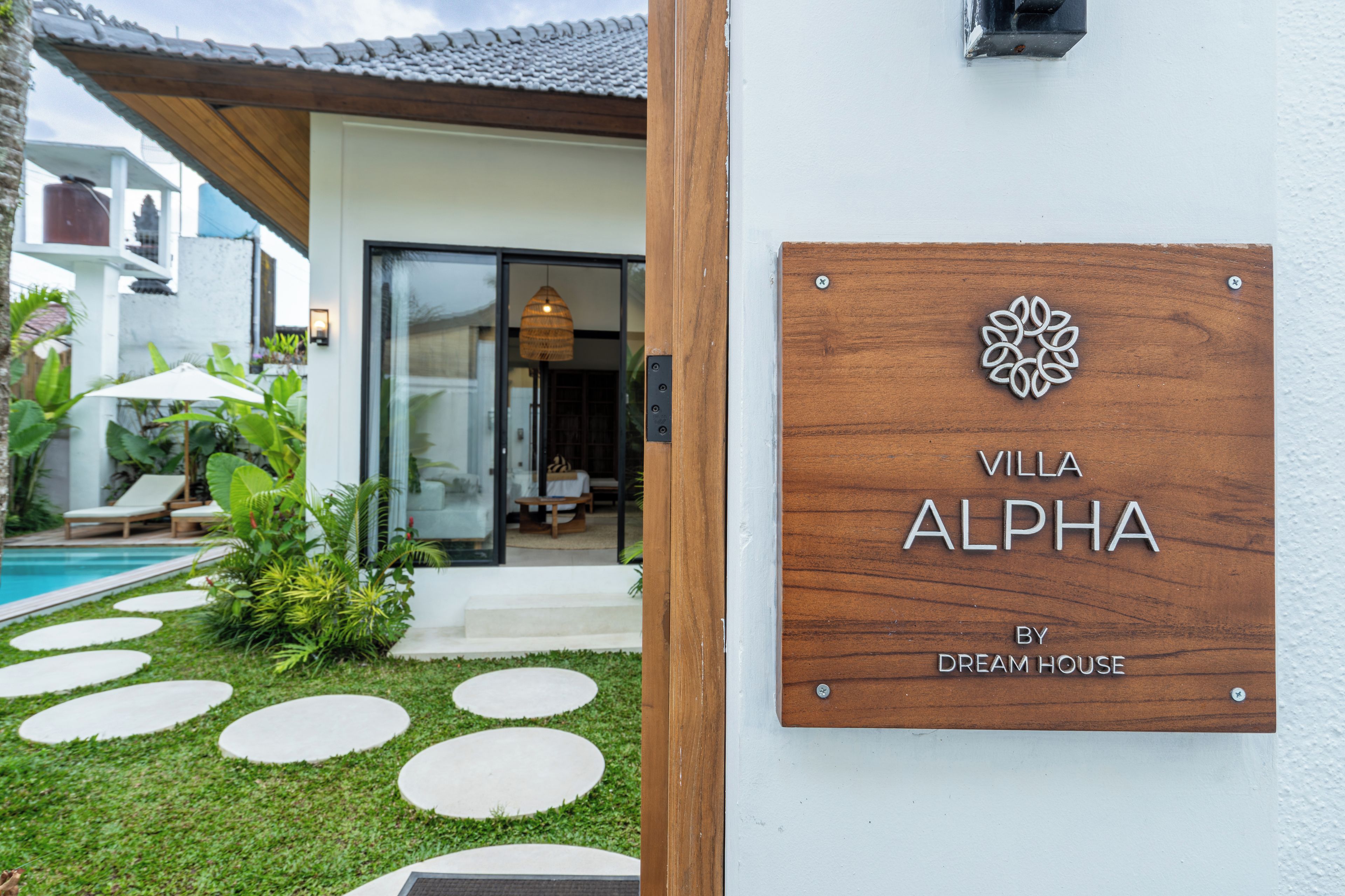 Una villa llamada "Villa Alpha" con un letrero de madera, una piscina y un jardín bien cuidado.