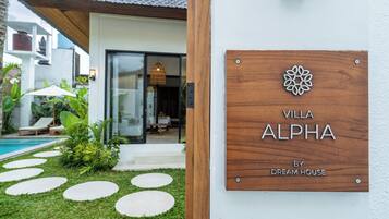 Una villa llamada "Villa Alpha" con un letrero de madera, una piscina y un jardín bien cuidado.