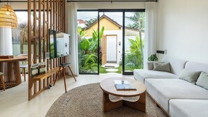 A modern living room with a sofa, coffee table, and TV stand. There is a sliding glass door leading to a garden.