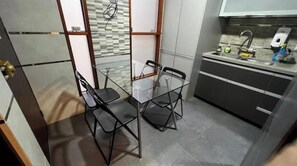 Une cuisine compacte avec une table et des chaises en verre, un évier avec un robinet et un dosseret carrelé.
