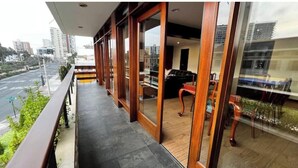 Un balcon donnant sur un paysage urbain, un banc en bois et une table à manger avec des chaises.