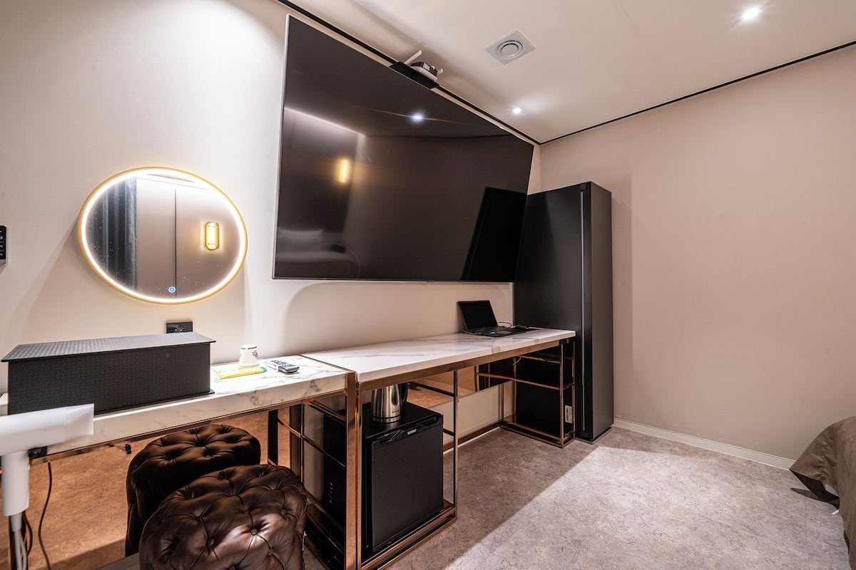 A modern room with a desk, a large flat-screen TV, a compact refrigerator, and a comfortable seating area.