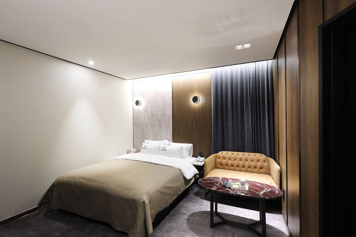 A hotel room with a bed, a chair, a desk, and a curtain.