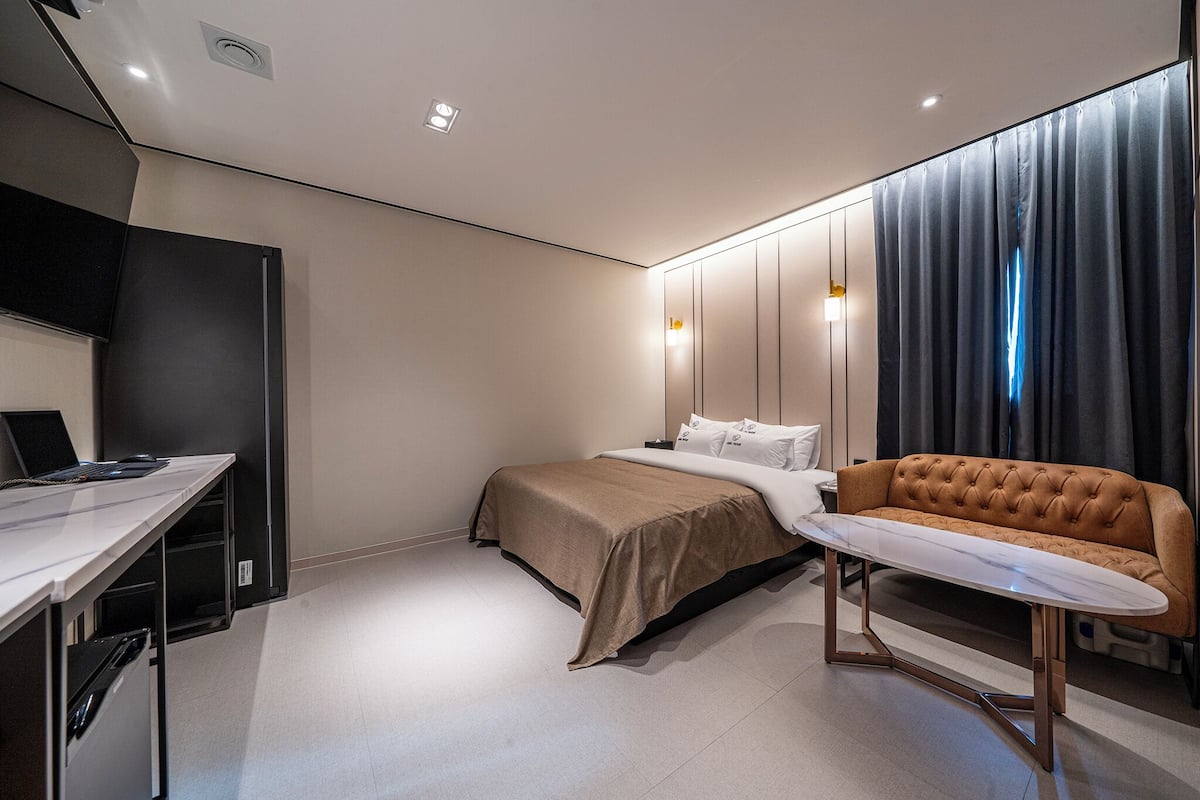 A modern hotel room with a bed, a desk, a sofa, and a TV.