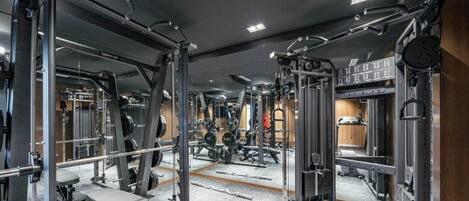Un gimnasio con equipo de ejercicio variado, paredes con espejos y una distribución limpia y ordenada.