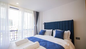 Une chambre d’hôtel avec un grand lit, une vue sur la ville depuis un balcon et une fenêtre avec des rideaux légers.