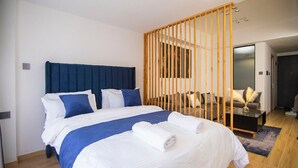 Une chambre d’hôtel moderne dotée d’un grand lit, d’une cloison en bois et d’un coin salon avec un canapé et des fauteuils.
