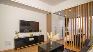 Un salon moderne avec une console noire, un canapé, un téléviseur fixé au mur et une cloison en bois.
